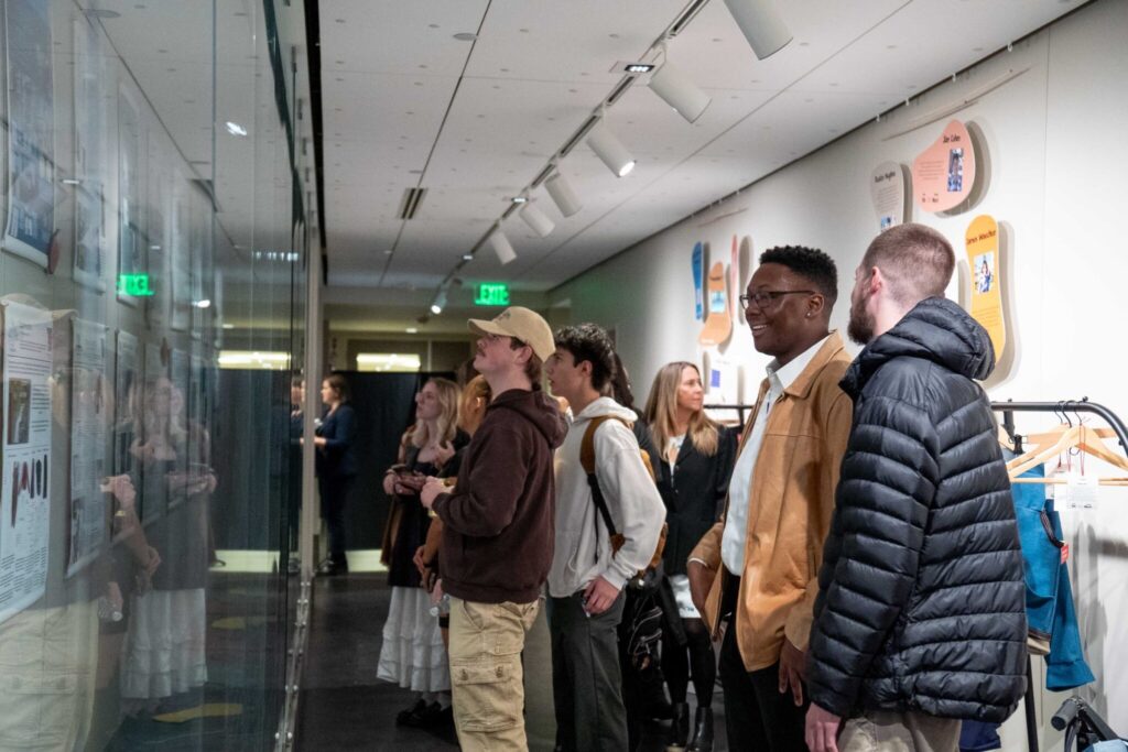 a large group of about 9 people stand in the hallway admiring the posters on exhibition