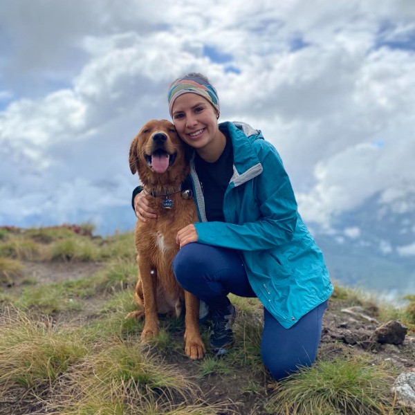Savannah Guy poses with her golden retriever on a hike. She is wearing a blue jacket and a colorful headband.