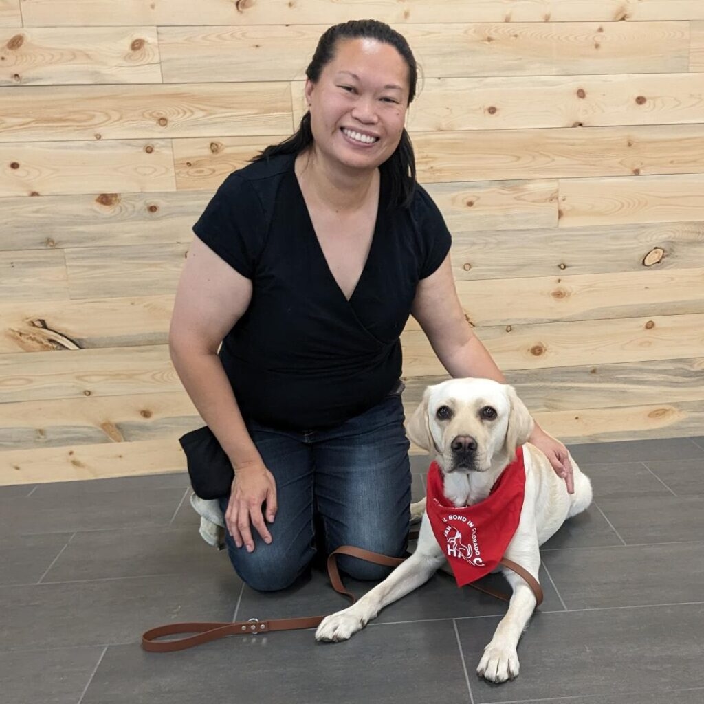 human-animal bond in colorado volunteer nancy loos and her yellow lab havarti at their certification evaluation day smiling and with havarti wearing a red habic bandana