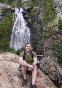 Aaron Nacey poses on a rock in front of a waterfall.