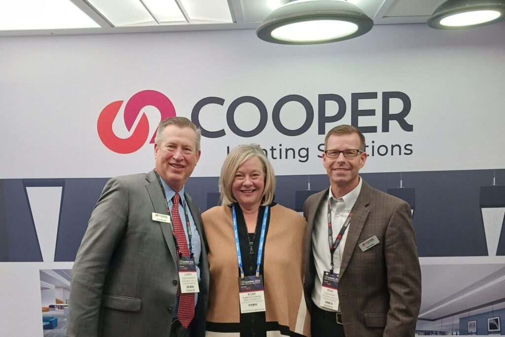 Kami Stutzman stands in the center with associates from Cooper Lighting Solutions on either side of her in front of the Cooper Lighting Solutions sign