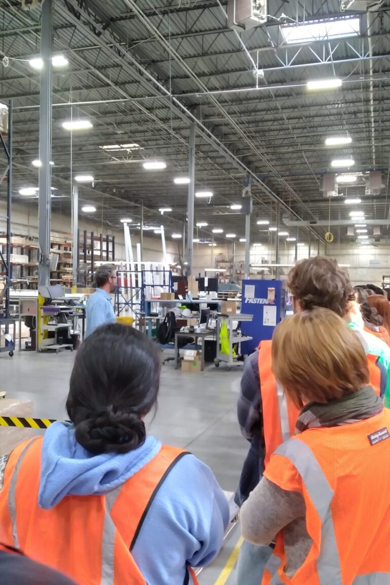 3 students wear orange vests and lookout over the vast cooper lighting warehouse