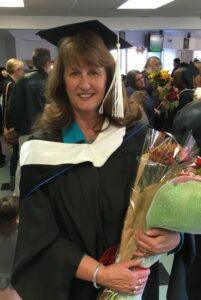 Michele wears a graduation gown and holds flowers.