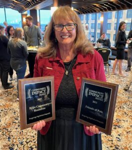 Michele holds up 2 separate awards which each read "Community Impact Awards 2023" followed by "Hope Community Resources" and "Friends of Pets".