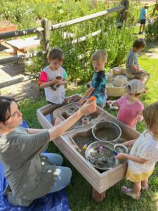 Kids play outside around a sensory table with mud and sand.