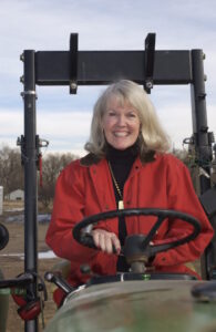 Buchan sits in the drivers seat of a tractor wearing an red blazer. 