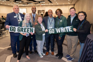Heather with other leaders from Michigan State at the 2024 ACPA conference in Chicago, holding small banners that say "go green" and "go white."