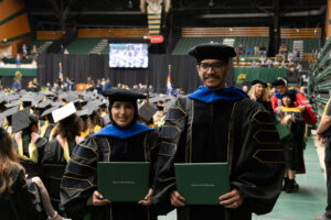 Rana Alarawi and Rayyan Bukhari, a married couple, pose for a photo on the floor of Moby Arena during commencement and after they received their diplomas