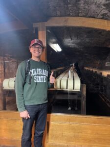 Man in a Colorado State University sweater stands in front of a cheese cellar