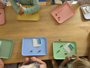 Multiple colored trays alongside children sit at a table