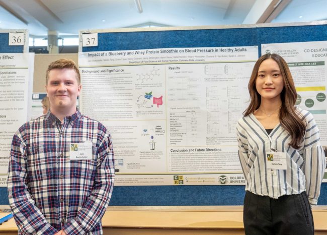 Jack smiles with his research partner in front of their research poster.