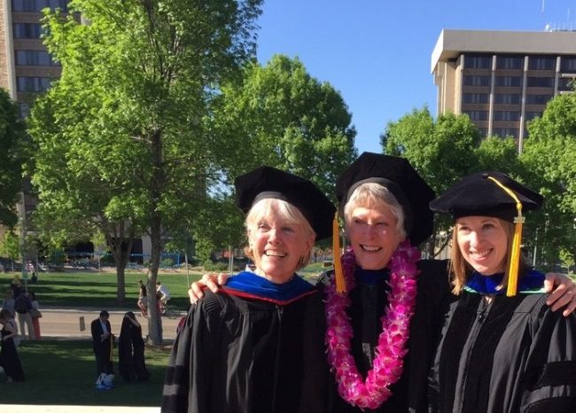 Vicky Buchan smiles with a faculty member and a graduating Ph.D. student in graduation gowns.